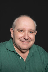 Portrait of a sexagenarian man dressed in a green polo shirt, with gray hair and blue eyes, looking at smiling camera with relaxed and happy expression. Concept of aging