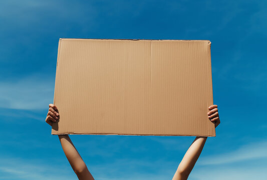 hands holding up a blank cardboard sign on clear blue sky background