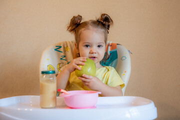 A little girl is sitting on a high chair and eating a green apple