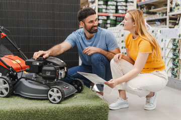 Happy couple examining new model of lawn mower in an electrical store for gardeners
