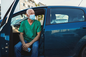Naklejka premium A photo of a mature male doctor sitting in his car wearing a protective mask and looking at his phone. A male nurse sits in a car and texting on his mobile phone.