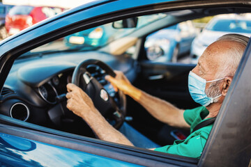 Confident medical worker wearing medical scrubs and protective face mask while driving a car during the day. Mature male healthcare professional drives to work.