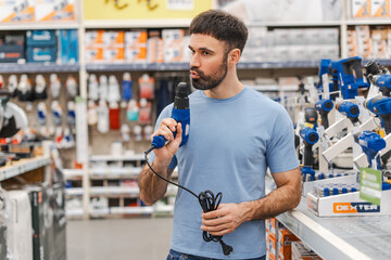 Young man holding modern electric drill standing in tool store