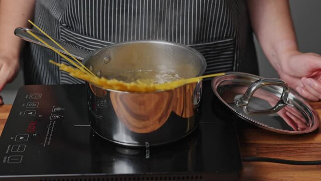 A woman throws spaghetti into a pot of boiling water