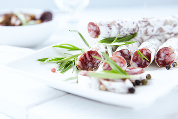 Sliced french salami with fresh rosemary on white background. Copy space.