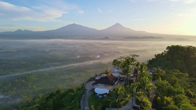 Aerial view of Enam Langit Restaurant on the top of Menoreh Hill in sunny morning and mountain range on the horizon.