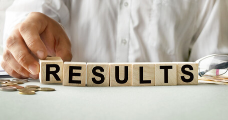 RESULTS inscription on the texture of wooden cubes. A business man holds a cube in his hand. An inscription on a financial, business or economic theme.