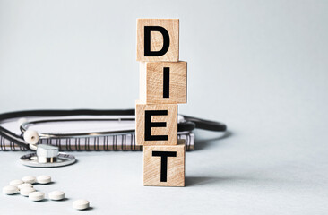 DIET inscription on wooden cubes isolated on white background, medicine concept. Nearby on the table are a stethoscope and pills.