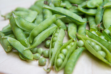 Freshly gathered pea pods , some open with seeds visible, on a wooden tray