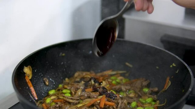 Adding thick, dark sauce to Asian food. Add unagi sauce. Teriyaki sauce. man's hand holds a spoon and adds a tablespoon of sauce.