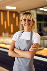 A smiling female worker, posing for the camera, wearing an apron, working at the bakery.