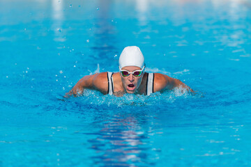 Female swimmer practices dolphin technique in outdoor pool. Swimming style, fitness, water sport, active woman, healthy lifestyle