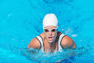 Female swimmer demonstrating breaststroke in outdoor pool. Swimming technique, active woman, water...