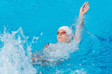 Female swimmer demonstrating breaststroke in outdoor pool. Swimming technique, active woman, water...