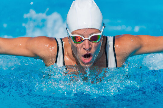 Female swimmer practices dolphin technique in outdoor pool. Swimming style, fitness, water sport, active woman, healthy lifestyle