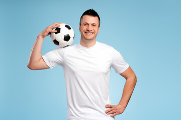 Handsome sportsman smiling and holding soccer ball on blue background