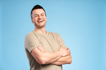 Smiling man in pastel t-shirt with arms crossed, close-up, looking at camera posing in studio