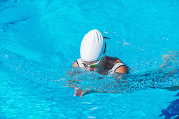 Female swimmer demonstrating breaststroke in outdoor pool. Swimming technique, active woman, water sport, fitness, healthy lifestyle