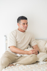 Fototapeta premium A Chinese Malaysian man in his 20s wearing casual, warm-colored clothing, playing with a cat around the bed in his home in Malaysia