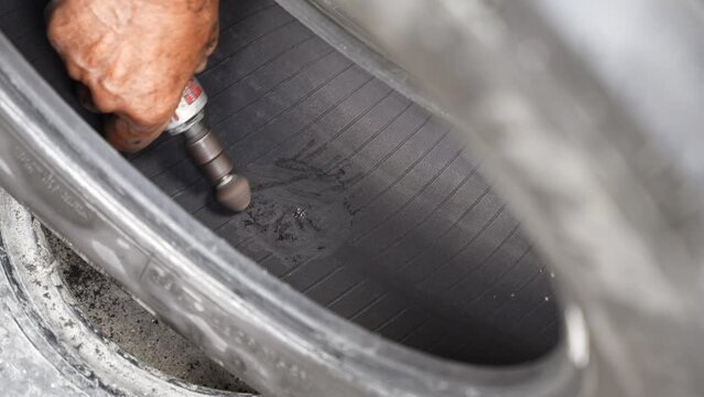 Car mechanic repairs punctured tire hit by nail on rim in service workshop. Close-up of a mechanic at a tire service shop changing a tire.