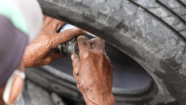 Car mechanic repairs punctured tire hit by nail on rim in service workshop. Close-up of a mechanic at a tire service shop changing a tire.