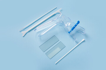 Gynecological speculum with pap smear test tools on blue background