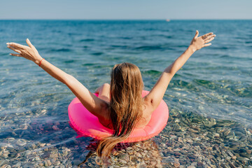 A woman is floating on a pink inflatable raft in the ocean