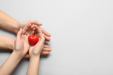 Hands of woman and child with red heart on grey background