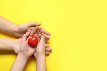 Fototapeta premium Hands of woman and child with red heart on yellow background