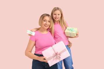 Beautiful young woman and her cute little daughter with gift boxes on pink background