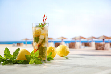 Image of copy space for drinks and food and products. Glass of mineral water with lemon slices, ice and straws on white table with blurred seascape and tropical beach background.