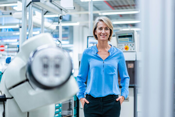 Happy businesswoman standing with hands in pockets at factory