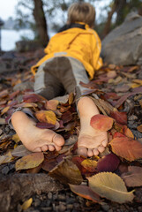 barefoot child lies on ground strewn with multi-colored leaves in park. carefree childhood, relaxation, enjoy warm autumn. children in nature, Indian summer. Hello, Autumn. seasonal atmospheric photo