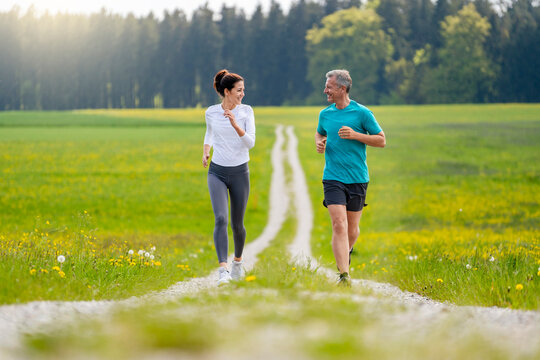 Smiling man and woman running together on footpath near meadow