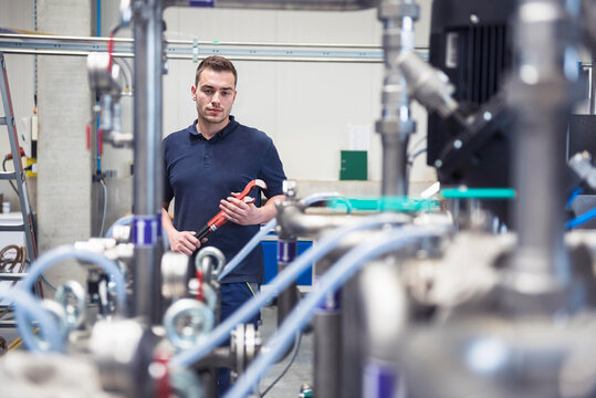 Engineer holding wrench and examining machine at industry