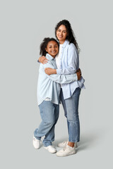 Beautiful young happy African-American mother with her daughter hugging on grey background