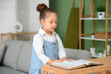 Cute little girl reading Holy Bible at home