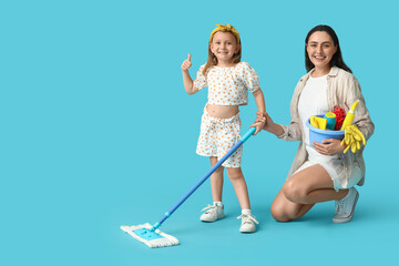 Happy mother and her daughter with different cleaning supplies showing thumb-up gesture on blue background
