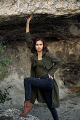 Woman in green jacket and black jeans poses against majestic rocky landscape