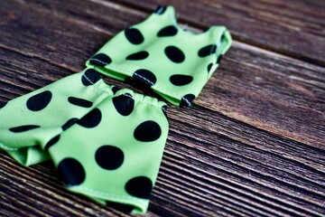 Green polka dots sleeveless top shirt and short pants set. Small human doll fashion clothing object isolated on dark wooden surface table background. © Amanda Alamsyah