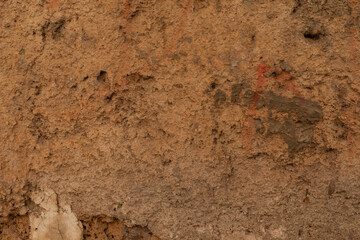 A rough textured wall with patches of reddish brown paint