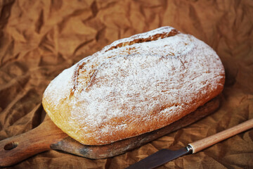 Homemade grain bread on a wooden board next to a knife on a linen napkin
