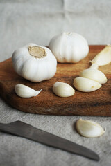 Whole garlic and cloves on a wooden board next to a knife on a linen napkin