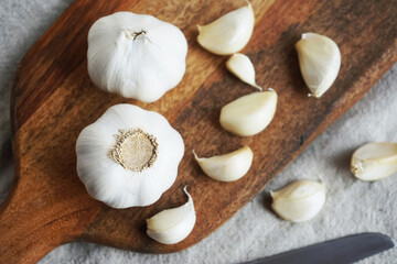 Whole garlic and cloves on a wooden board next to a knife on a linen napkin