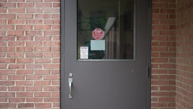 Camera pulling away from school wire reinforced door with STOP sign for security and stating it is under video surveillance.