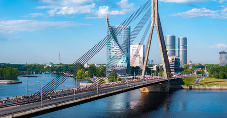 Aerial shot of runners participating in a marathon on a cable-stayed bridge in Riga, Latvia. The city skyline and calm river create a picturesque backdrop.