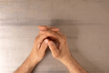 Two hands resting on a table their fingers intertwined