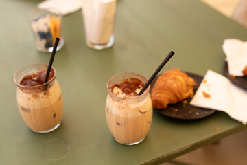 Two iced coffees and a croissant on a green table