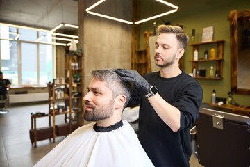 Experienced hair stylist adding last touches to stylish client's hairstyle