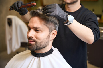 Barber using round hairbrush to modeling handsome man hairstyle